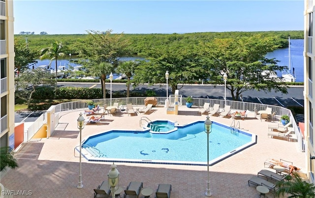 view of pool with a patio, a water view, fence, and a pool with connected hot tub