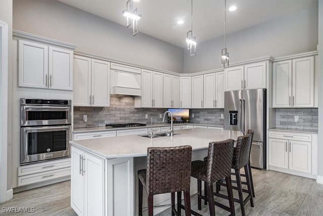 kitchen with sink, a center island with sink, white cabinetry, stainless steel appliances, and custom range hood