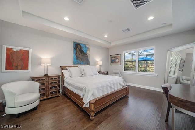 bedroom with a raised ceiling, visible vents, dark wood finished floors, and baseboards