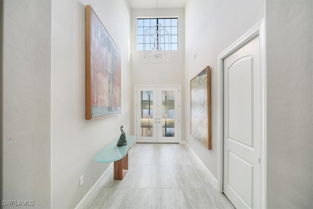 doorway to outside featuring french doors, light tile patterned floors, a towering ceiling, a chandelier, and baseboards