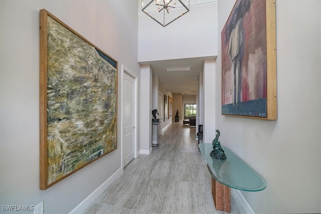 hallway featuring an inviting chandelier, light wood-type flooring, and a high ceiling