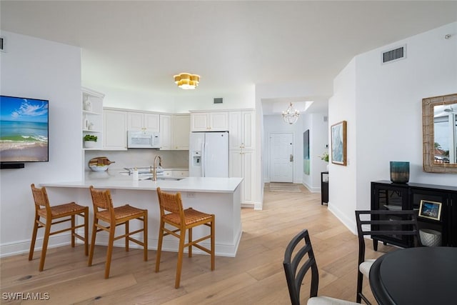 kitchen with decorative light fixtures, white cabinetry, sink, kitchen peninsula, and white appliances