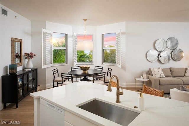 kitchen featuring pendant lighting, sink, white dishwasher, light hardwood / wood-style floors, and white cabinets