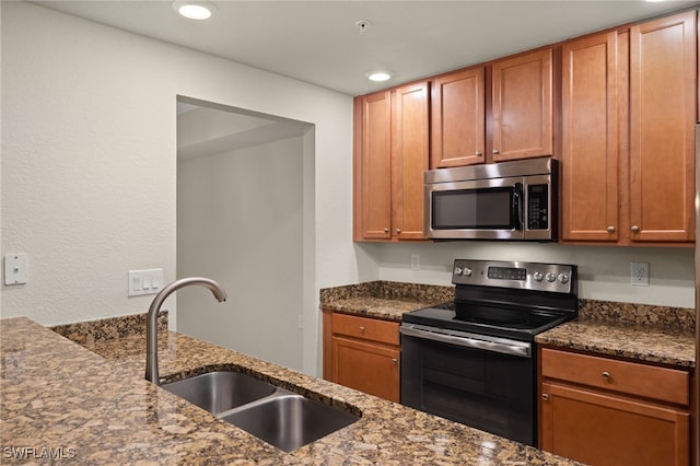 kitchen with appliances with stainless steel finishes, sink, and dark stone countertops