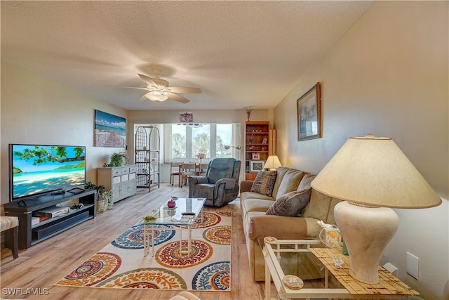 living room with a textured ceiling, ceiling fan, and light hardwood / wood-style flooring