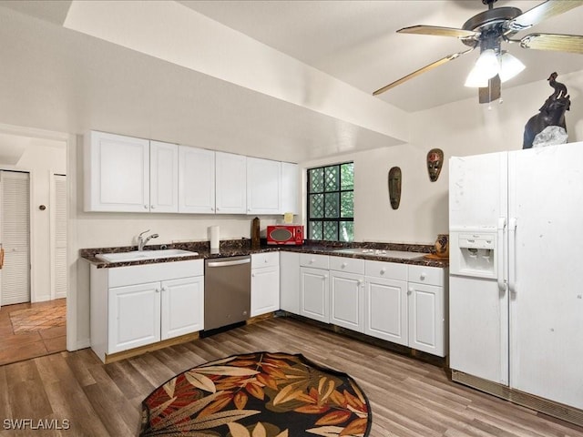 kitchen with dark countertops, dark wood-style flooring, stainless steel dishwasher, white fridge with ice dispenser, and a sink