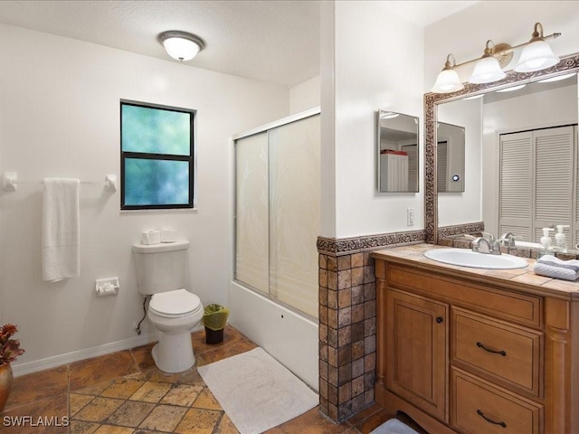 full bath featuring shower / bath combination with glass door, stone tile flooring, vanity, and toilet