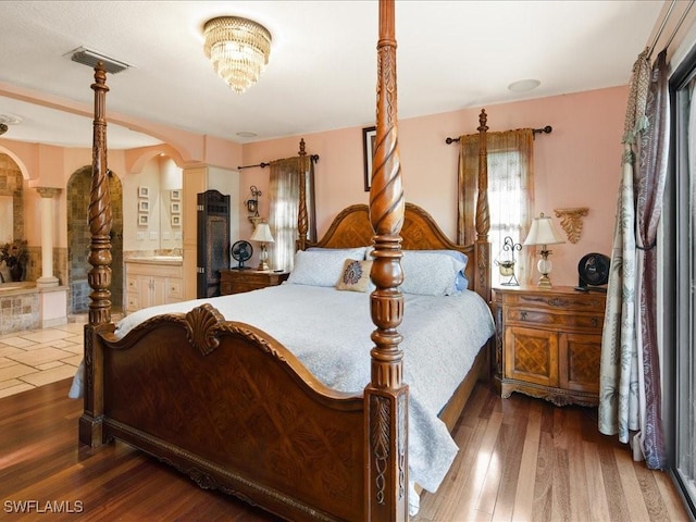 bedroom with arched walkways, visible vents, ensuite bathroom, and wood finished floors