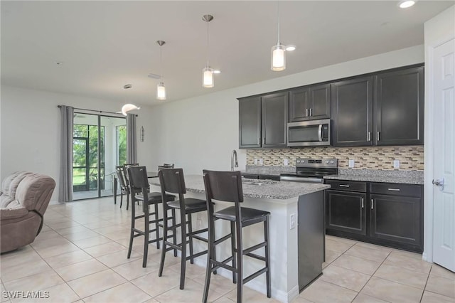 kitchen with a breakfast bar, light stone counters, decorative light fixtures, appliances with stainless steel finishes, and an island with sink