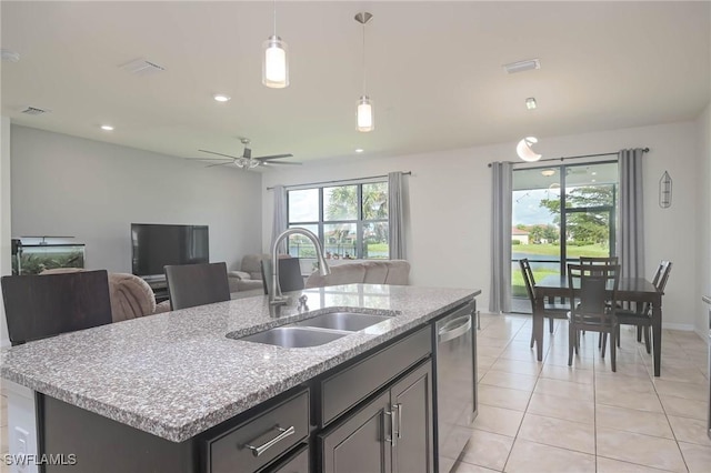 kitchen with sink, dishwasher, light stone countertops, a center island with sink, and decorative light fixtures