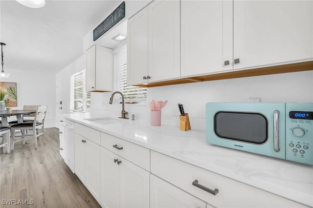 kitchen with sink, light hardwood / wood-style flooring, white cabinetry, hanging light fixtures, and light stone countertops