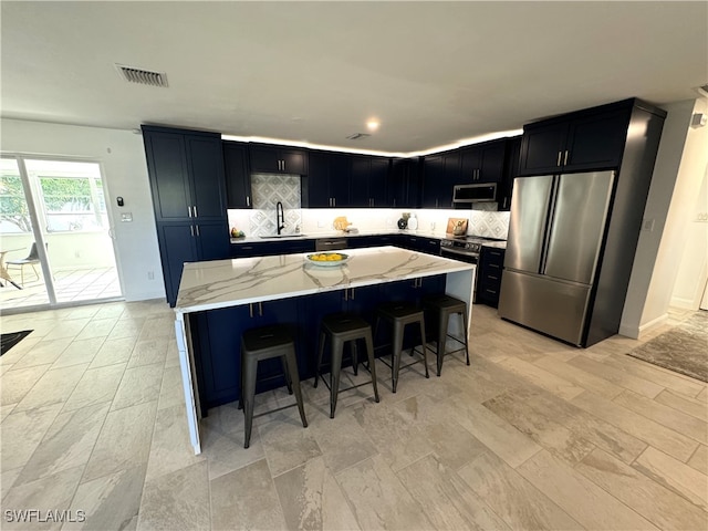 kitchen with stainless steel appliances, sink, a breakfast bar, light stone counters, and a kitchen island