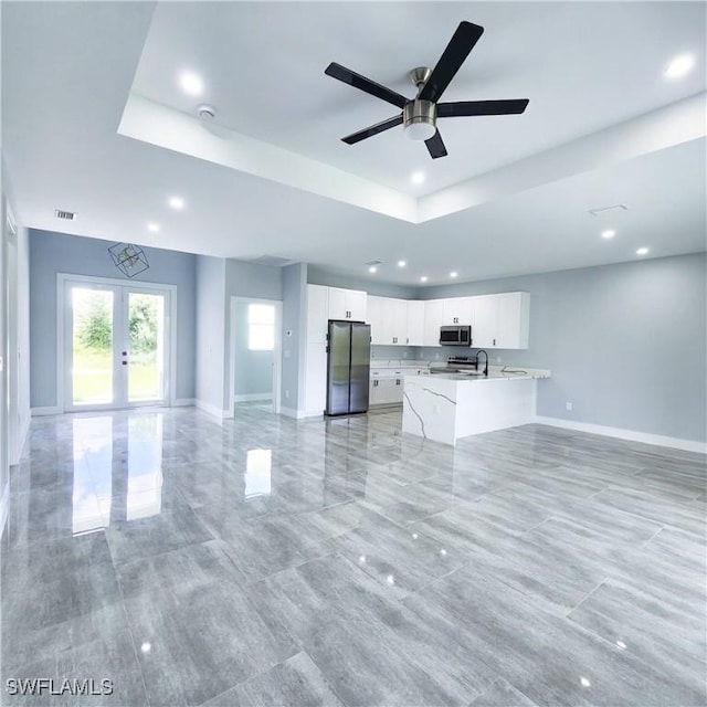 unfurnished living room with ceiling fan, sink, a raised ceiling, and french doors