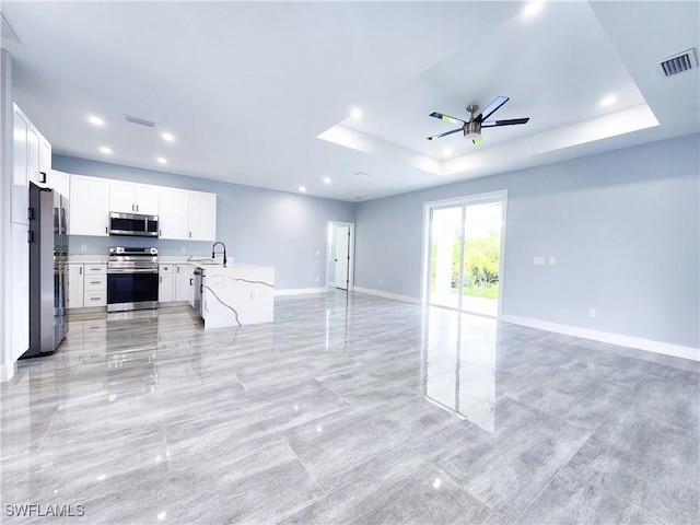 kitchen featuring appliances with stainless steel finishes, sink, light stone counters, white cabinets, and a raised ceiling