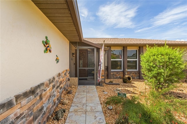 entrance to property with stucco siding, stone siding, and roof with shingles