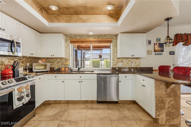 kitchen featuring a tray ceiling, a peninsula, stainless steel appliances, white cabinetry, and a sink