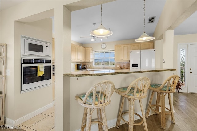 kitchen featuring a kitchen breakfast bar, decorative light fixtures, light wood-type flooring, white appliances, and light brown cabinetry