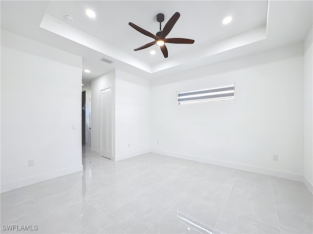 empty room featuring ceiling fan, a raised ceiling, and light tile patterned floors