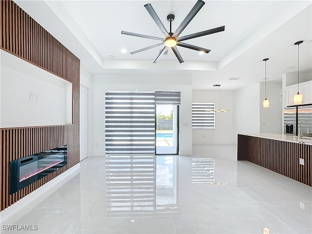 tiled living room with ceiling fan, sink, and a tray ceiling