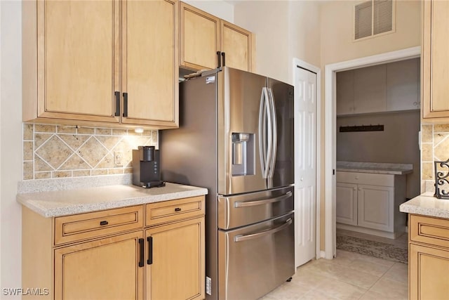 kitchen featuring backsplash, light brown cabinetry, light stone counters, light tile patterned floors, and stainless steel fridge