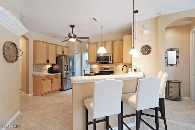 kitchen with light brown cabinets, decorative backsplash, appliances with stainless steel finishes, decorative light fixtures, and light tile patterned flooring