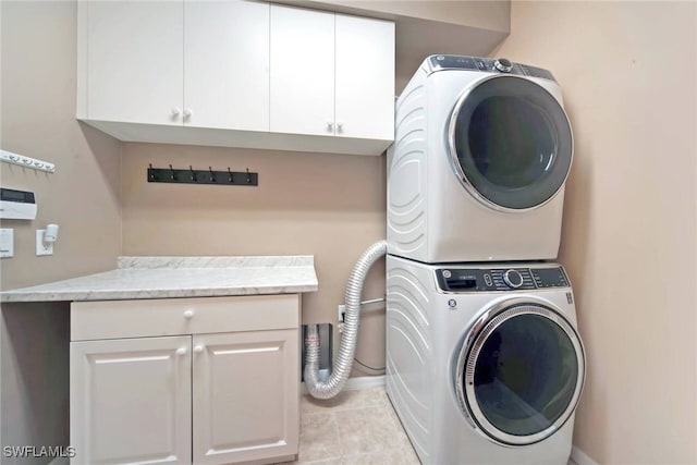 laundry area featuring stacked washing maching and dryer, light tile patterned floors, and cabinets