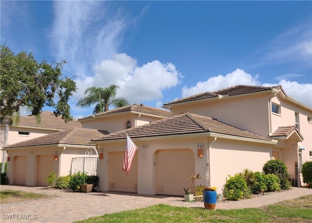 mediterranean / spanish-style house with a garage, decorative driveway, a tile roof, and stucco siding