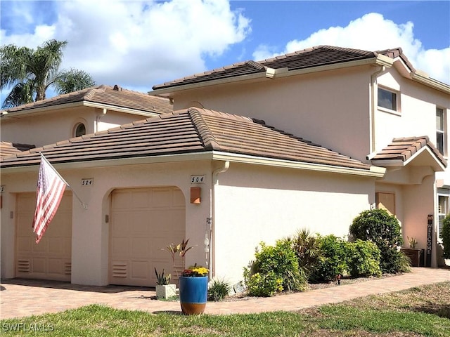 view of home's exterior featuring decorative driveway, a tile roof, an attached garage, and stucco siding