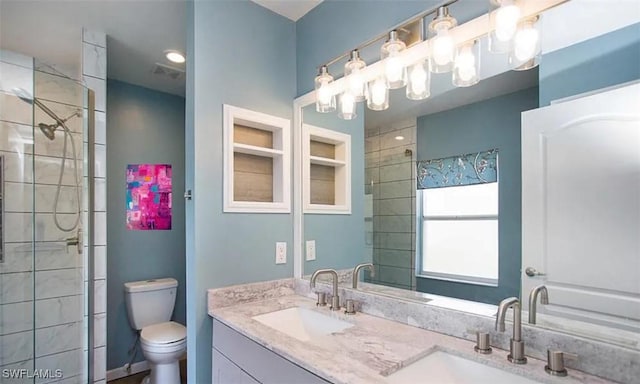 full bathroom with double vanity, tiled shower, a sink, and toilet