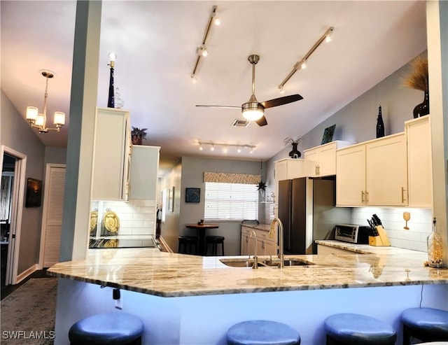 kitchen featuring visible vents, freestanding refrigerator, a peninsula, vaulted ceiling, and a sink