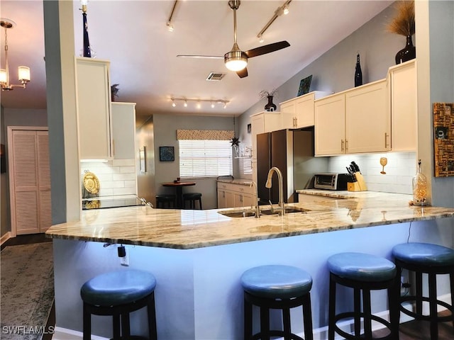 kitchen with decorative light fixtures, visible vents, vaulted ceiling, a sink, and a peninsula