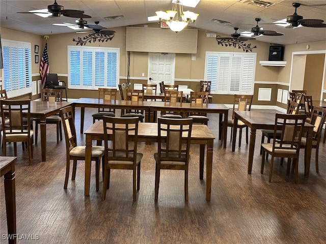 dining area featuring a drop ceiling, ceiling fan with notable chandelier, and dark hardwood / wood-style floors