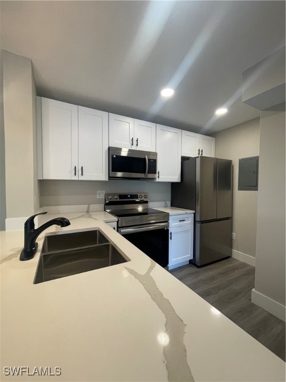 kitchen featuring stainless steel appliances, white cabinets, sink, light stone countertops, and dark wood-type flooring