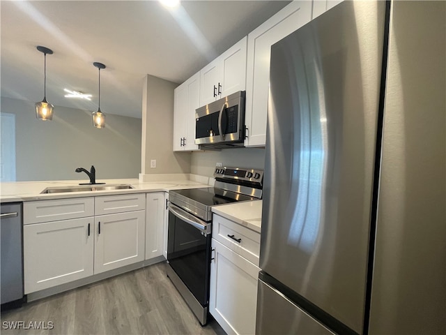 kitchen with light hardwood / wood-style flooring, white cabinets, stainless steel appliances, pendant lighting, and sink