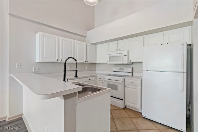 kitchen with white appliances, sink, kitchen peninsula, light tile patterned floors, and white cabinetry