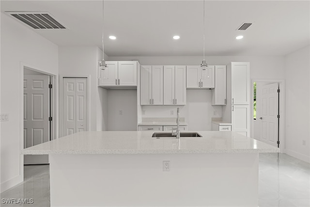 kitchen featuring sink, decorative light fixtures, white cabinetry, and an island with sink