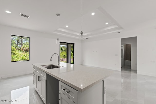 kitchen with sink, a center island with sink, light tile patterned floors, a tray ceiling, and hanging light fixtures