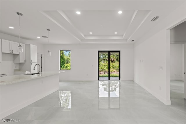 unfurnished living room with light tile patterned flooring, sink, and a tray ceiling