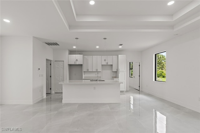 kitchen with light tile patterned floors, a raised ceiling, pendant lighting, and an island with sink