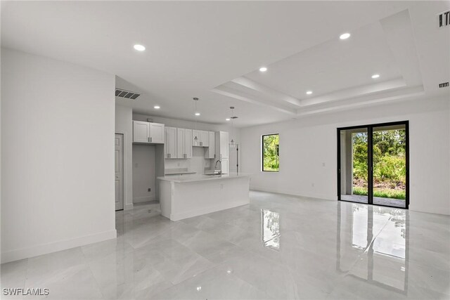 unfurnished living room with a raised ceiling, light tile patterned flooring, and sink