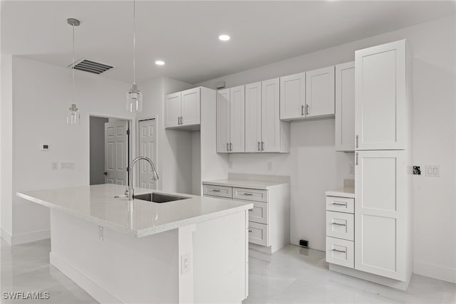 kitchen with sink, pendant lighting, white cabinets, and an island with sink