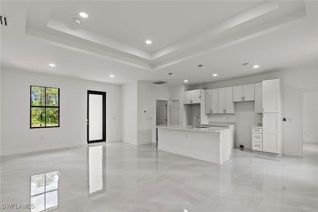 kitchen featuring white cabinets, a raised ceiling, an island with sink, and light tile patterned floors