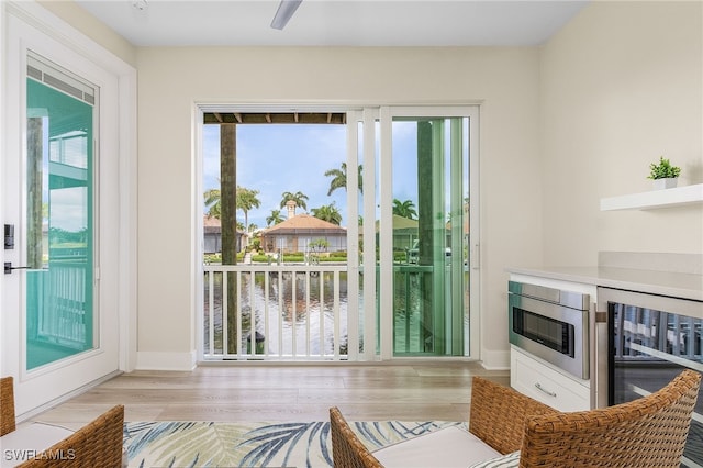 doorway with wine cooler, a water view, light wood-type flooring, and a wealth of natural light