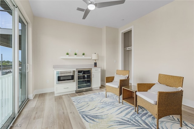 living area featuring beverage cooler, ceiling fan, and light wood-type flooring