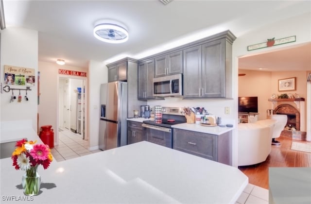 kitchen with gray cabinets, a brick fireplace, stainless steel appliances, and light hardwood / wood-style floors