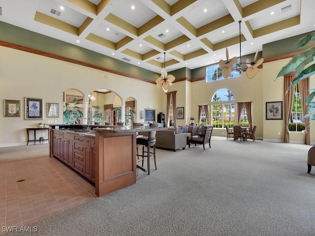 kitchen featuring light carpet, a kitchen bar, a towering ceiling, a large island with sink, and plenty of natural light