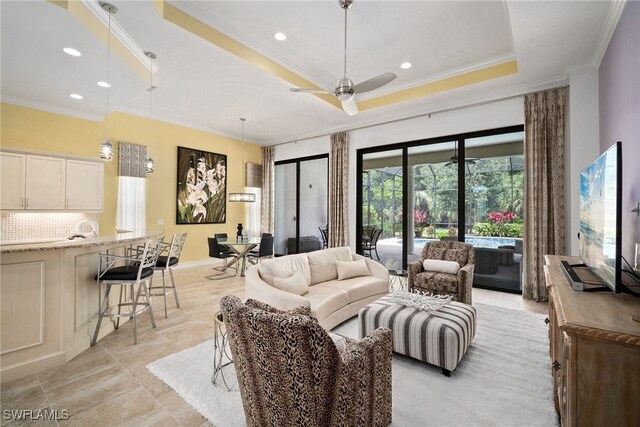 living room featuring ceiling fan, ornamental molding, and a raised ceiling