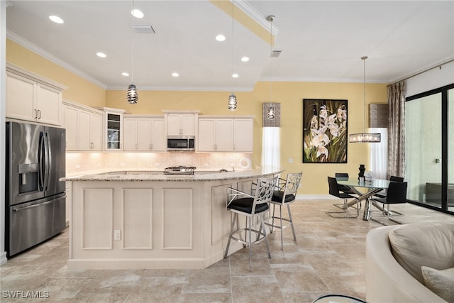 kitchen with stainless steel appliances, light stone counters, hanging light fixtures, an island with sink, and ornamental molding