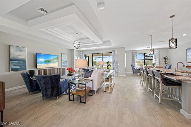 living area with visible vents, light wood-type flooring, a tray ceiling, baseboards, and a chandelier