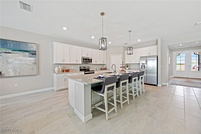 kitchen with stainless steel appliances, white cabinets, light stone counters, french doors, and an island with sink